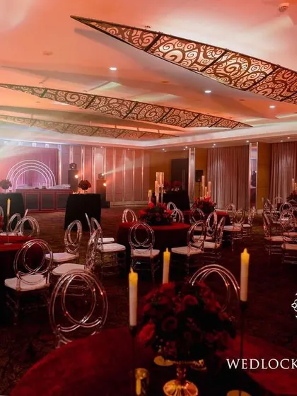 A bold and luxurious reception with a red and black color scheme. The decor includes rich red roses, modern crystal candelabras, and a stylish bar with a neon arch backdrop.