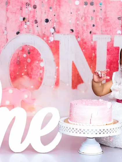 A perfect "look at me" moment. With frosting on her fingers and a huge smile, this is what a successful first birthday cake smash looks like.