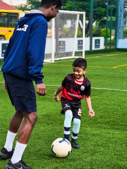 The joy of learning. A young player smiles as he practices his dribbling skills with one of our coaches.