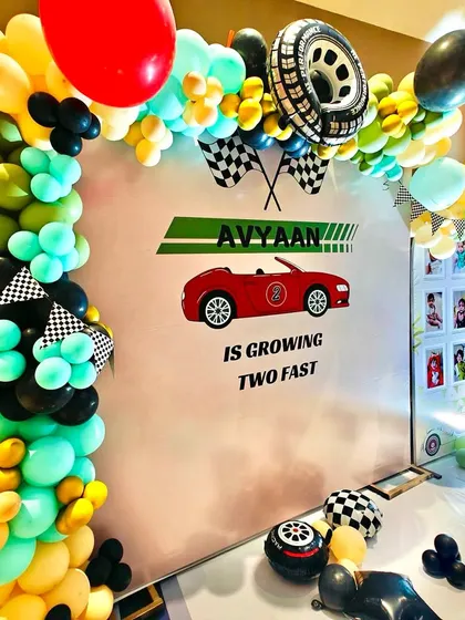 A close-up of the 'Growing Two Fast' backdrop, framed by a colorful balloon garland with checkered flags and a tire foil balloon.