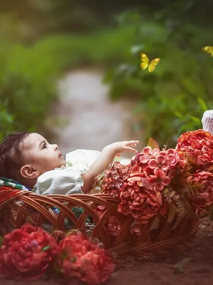 A six-month-old baby lies in a basket adorned with flowers, gazing at butterflies. This composite image combines a beautiful portrait with a magical, storytelling element.