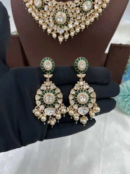 The Zarista Premium Moissanite Necklace set, shown here in both ruby and green variations. This set includes a necklace, maang tikka, and earrings, featuring large central stones surrounded by detailed craftsmanship.