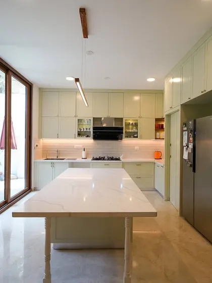 A wider view of the sage green kitchen, showing how the large glass doors connect the space to the outdoors, flooding it with natural light and creating a seamless indoor-outdoor flow.