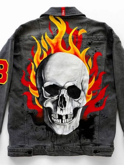 This is the full view of a custom hand-painted denim jacket featuring a flaming skull. The design includes patches on the front and sleeve, creating a cohesive, edgy look.