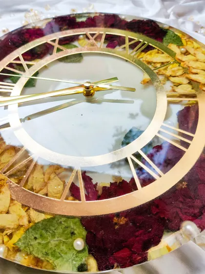 A close-up of the finished resin clock, adorned with delicate varmala flowers. The gold Roman numerals and hands add a touch of timeless elegance to this custom piece.