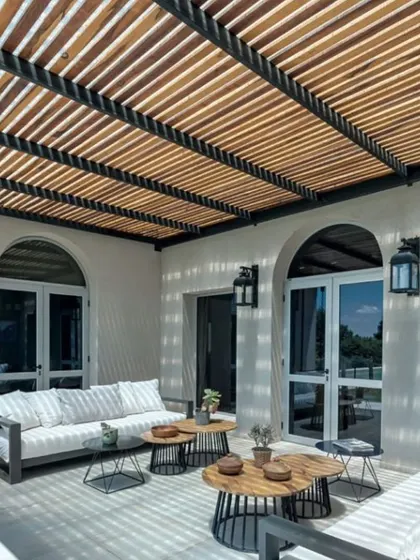 A stylish rafter pergola provides filtered sunlight for this chic patio seating area. The design complements the modern architecture of the home, creating an inviting and comfortable space for outdoor relaxation.