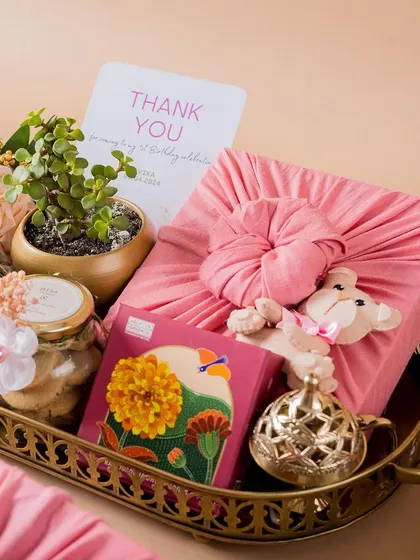 A beautiful thank you hamper arranged on a brass tray, featuring a live plant, gourmet cookies, and products wrapped in pink Furoshiki fabric.