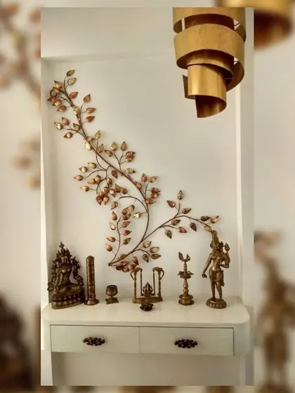 We create serene and spiritual corners with carefully chosen art and decor. This display features brass idols and a beautiful metal wall sculpture of a branching vine, all set against a clean white backdrop.