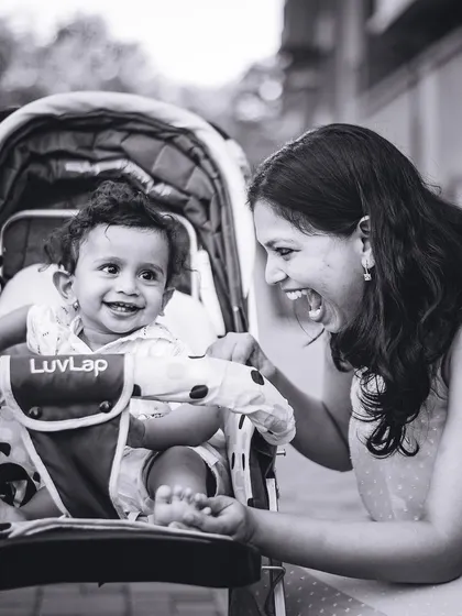 A candid black and white photo of a mother sharing a laugh with her baby, who is sitting in a stroller. These everyday moments are truly precious.