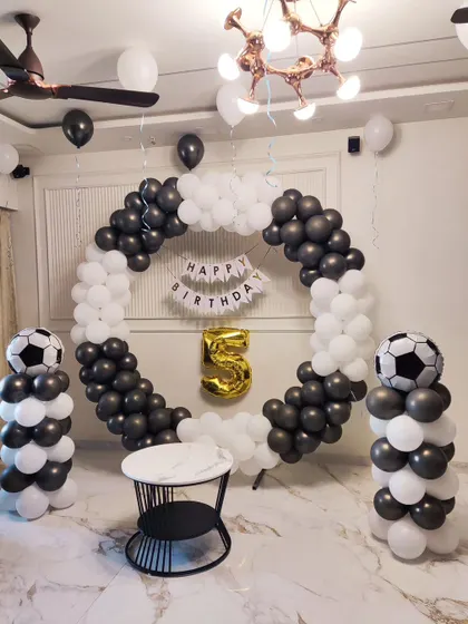 For a 5th birthday, I designed this sharp football-themed decoration. The setup uses a black and white balloon ring, matching balloon pillars topped with football balloons, and a gold '5' foil balloon to bring the sporty theme to life.