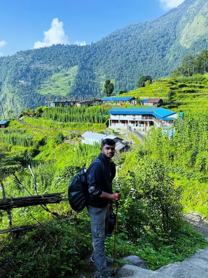 A trekker pauses on the trail to look back at the terraced fields and villages of the lower Annapurna region, showcasing the cultural landscape of the trek.