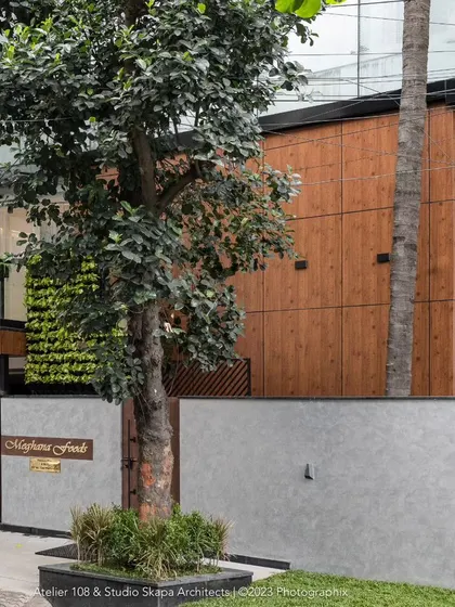 The facade of the Meghana Foods corporate office, a project transformed from a bare structure into a luxurious design statement. The design combines wood, concrete, and a vertical garden to create a lush and elite presence on a tree-lined avenue.