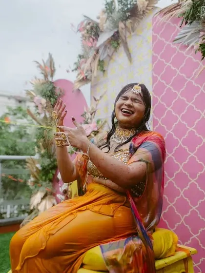 The bride laughs with joy during her outdoor Haldi ceremony, surrounded by beautiful pastel-themed decorations.