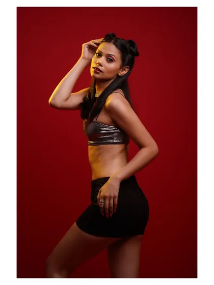 A high-energy studio shot with a bold red background. The metallic top and playful hairstyle create a fun and modern vibe.