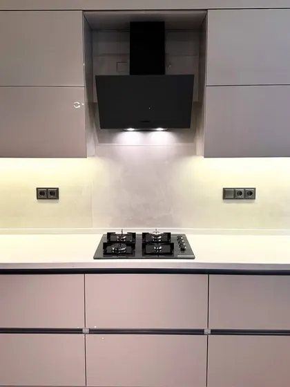 A focused shot on the cooking zone, featuring a modern black chimney and hob set against a subtle backsplash. The warm under-cabinet lighting provides excellent task illumination while enhancing the kitchen's sophisticated ambiance.