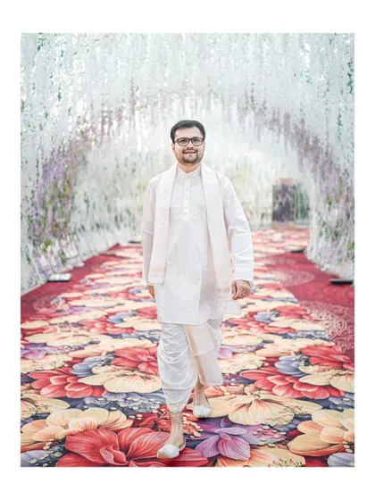 The groom makes his entrance, walking down a stunning floral carpet under an archway of white flowers at his Hubli wedding.