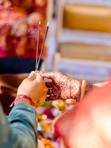 A close-up of the couple's hands holding incense sticks during a puja, a moment of shared prayer and new beginnings.