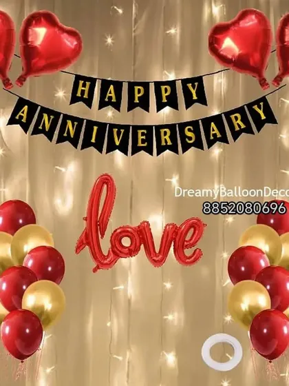 A simple and classic anniversary wall decoration. This kit includes a 'Happy Anniversary' banner, 'Love' foil balloon, and red and gold balloons against a fairy light curtain.
