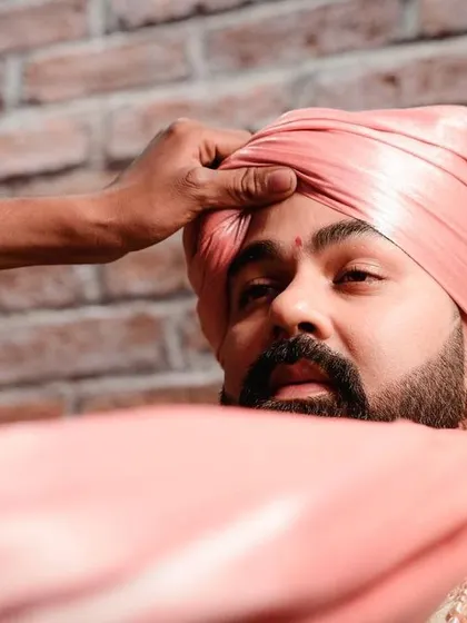 A candid moment of the groom getting ready. This photo captures the tying of the safa or turban, a significant ritual that is part of the groom's wedding preparations.