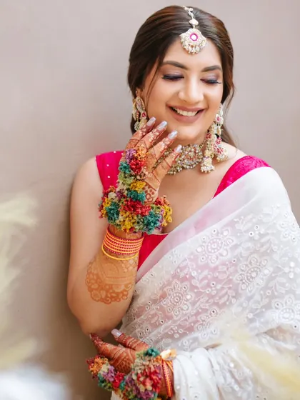 The bride's happy smile during her Haldi ceremony. She wears a chic white chikankari saree with a pop of fuchsia, accessorized with colorful floral jewelry.