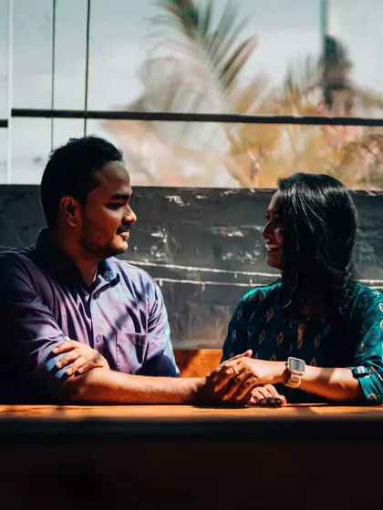 A couple shares an intimate moment across a table, the natural window light creating a soft and romantic mood for their pre-wedding photo.