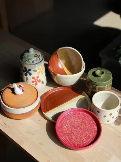 A vibrant collection of lidded jars, plates, and bowls, showcasing a variety of surface decoration techniques like stamping and hand painting.