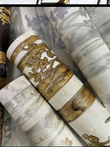 A collection of wallpaper rolls with a bamboo or tree bark design, featuring metallic gold and silver accents.