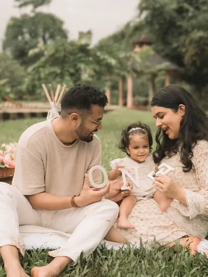 The family sits together on a blanket, interacting with the 'ONE' letters for their daughter's first birthday shoot.