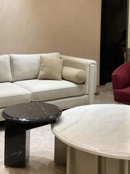 A close-up of our contemporary sofa with clean lines and a neutral fabric, paired with a black marble side table. This demonstrates our versatility in creating both bold and understated luxury pieces.