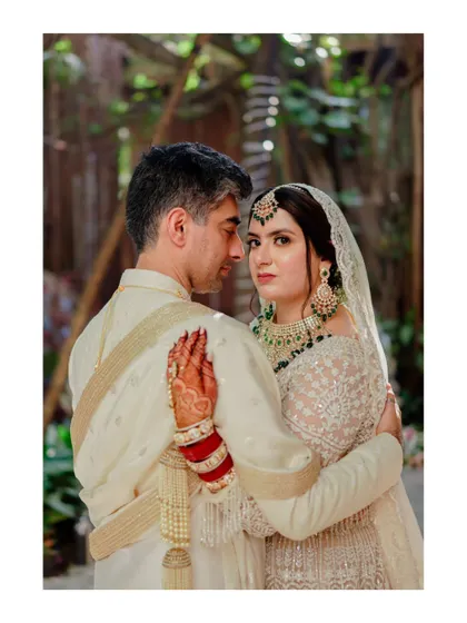 A classic, romantic portrait. The bride looks directly at the camera while embraced by her groom, a pose that is both intimate and engaging for the viewer.