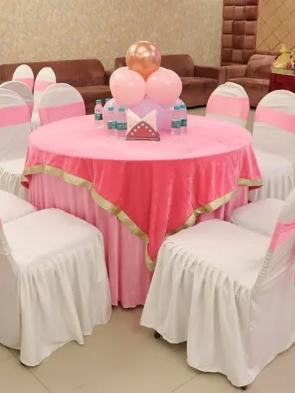 Guest table setup with pink tablecloths, white chair covers with pink sashes, and a simple balloon centerpiece.