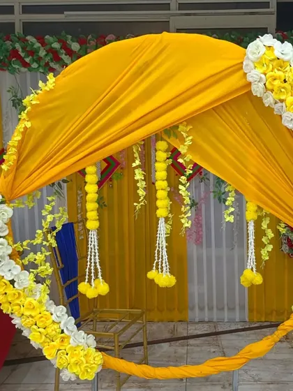 A close-up of a circular Haldi backdrop, showing how yellow fabric is draped within the frame and accented with marigold and white flower garlands.