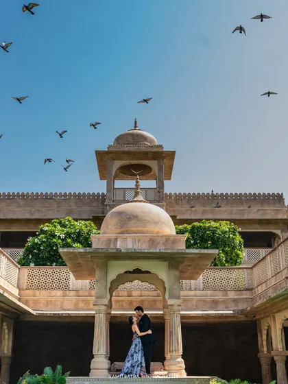 A romantic kiss framed perfectly within a domed structure at Fort Barwara, as birds fly across the blue sky.