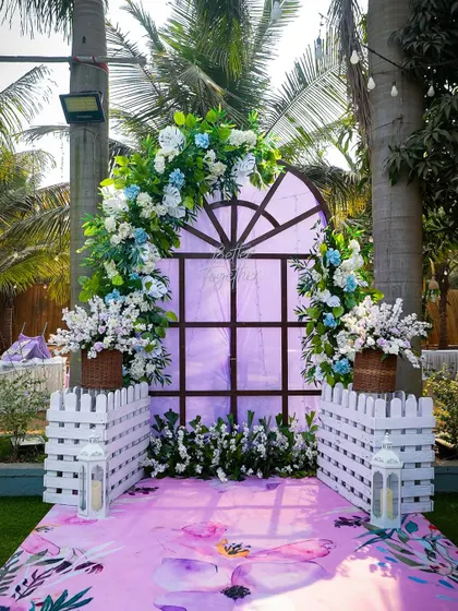 A full view of the charming photo corner. The window backdrop, picket fences, and floral carpet create a whimsical and picturesque spot for the couple and their guests.