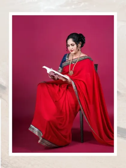 A thoughtful pose of a mother-to-be in a vibrant red saree, seated and reading a book. This styled studio shot adds a personal and narrative element to the maternity session.