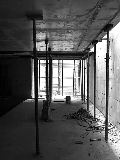 An interior space during construction, with temporary props supporting the freshly cast concrete ceiling slab. The light from an opening at the far end illuminates the raw interior.