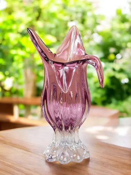 This elegant handblown glass vase is shaped like a blooming flower in a lovely shade of purple. Its organic form and beautiful color make it a perfect vessel for a small bouquet or a standalone art piece.