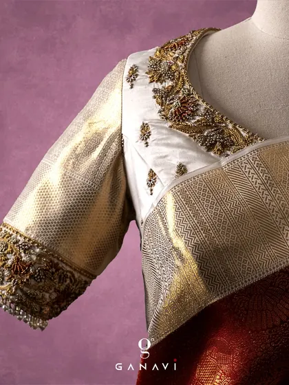 A detailed close-up of the ivory blouse, showing the delicate floral embroidery crafted with gold and maroon threads. The design is inspired by traditional motifs, given a fresh interpretation on the light-colored silk.