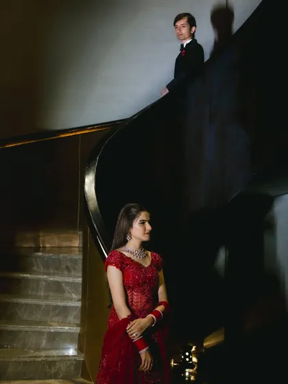 A modern fairytale. This artistic shot highlights the bride's stunning red gown and flawless makeup against a dramatic staircase, creating an epic wedding portrait.