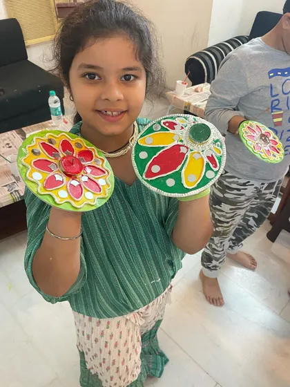 This happy student is holding up her two beautifully painted tea light holders. Her smile shows the fun and sense of accomplishment that comes from creating something with your own hands during our festive workshops.