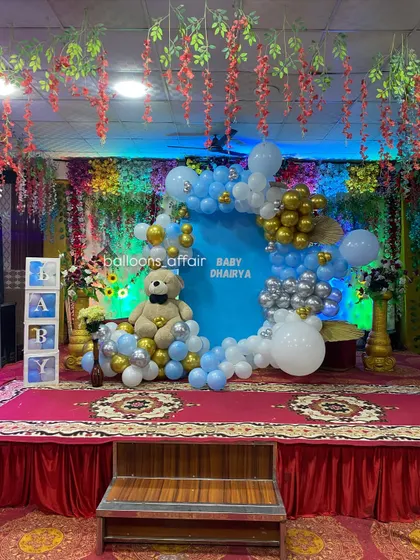 A full view of the banquet hall stage decorated for a baby's party. The setup includes a teddy bear theme, 'BABY' blocks, and floral arrangements on the side.