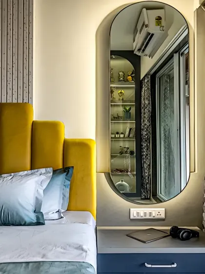 A close-up of a bedroom design showing a custom bedside table integrated with a vibrant yellow upholstered headboard. The backlit full-length mirror adds depth and functionality to the space.