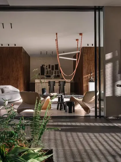 The main living room, featuring a mix of modern furniture and a statement orange light fixture. The space opens up completely to the outdoors, creating a seamless flow between the living area and the garden.