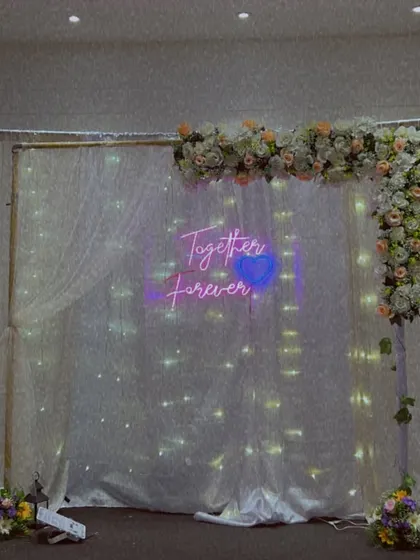 An elegant and simple backdrop perfect for an engagement or anniversary party. The sheer white drapes with fairy lights and a floral corner arrangement create a soft, romantic feel.