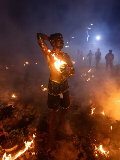 A wide shot of a Kulasai performer amidst the fires, giving a sense of the environment and the scale of the celebration.