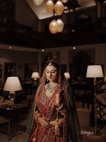 A sophisticated and moody bridal portrait. The bride is captured in a dimly lit, luxurious room, looking down at her lehenga.