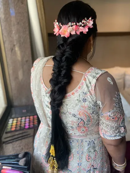 A stunning long fishtail braid adorned with a pink floral hair accessory and traditional parandi tassels.