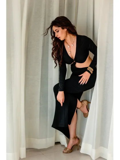 A black cutout dress shot against simple white curtains. The pose is dynamic and a little mysterious, using the curtains to frame the shot.