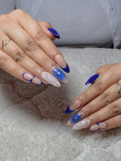 A striking design with a bold blue French tip, a sheer nude base, and a white floral pattern with blue and gold accents.