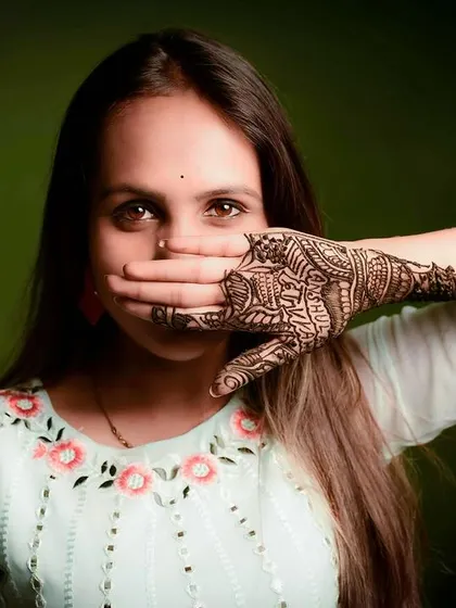 A creative portrait focusing on the bride's intricate mehndi design. Her expressive eyes peeking over her hand add a touch of mystery and allure to the photograph.